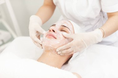Yüz bakımı prosedürleri. Güzellik uzmanı kozmetik kliniğinde güzel bir kadının yüzüyle masaj yapıyor.
