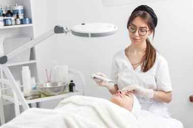 Kadın kozmetik uzmanı ultrasonik temizleme prosedürü uyguluyor. Güzellik salonunda genç bir kadın. Kozmetoloji ve profesyonel cilt bakımı kavramı