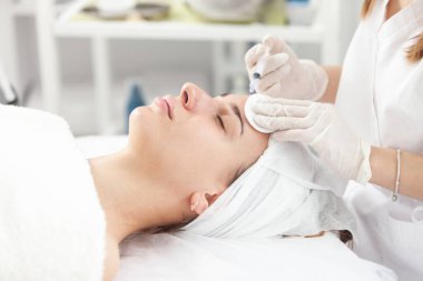 Yüz enjeksiyonu. Kozmetik Salonunda Yaşlanma Karşıtı Biorevalizasyon. Genç Güzel Kız Hyaluronic asit derisi alıyor. Şırıngada Doldurulmuş Güzellik Elleri