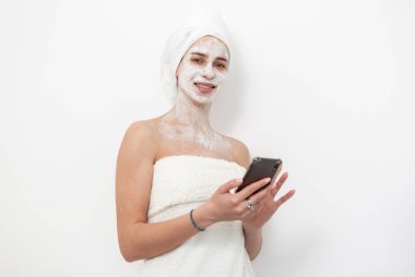 Yüz maskeli güzel bir kadın beyaz arka planda akıllı telefon kullanıyor. Cilt bakımı kavramı