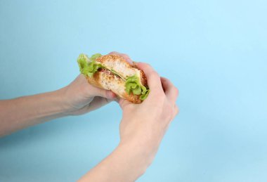 Mavi arka planda ısırılmış ev yapımı bir burger tutan eller.