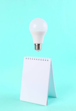 Mavi arka planda yüzen ampullü defter. Asgari fikir, ilham, kavram sanatı