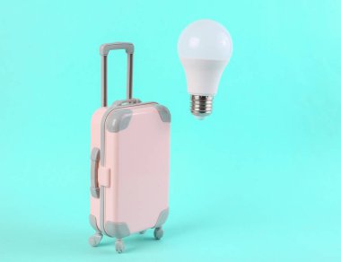 Oyuncak bavul ve mavi arka planda yüzen bir ampul. Asgari seyahat kavramı