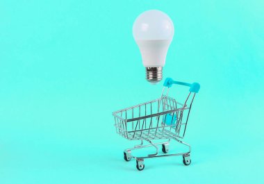 Mavi parlak arka planda yüzen ampullü alışveriş arabası. Asgari alışveriş kavramı