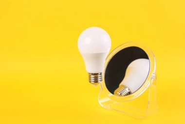 Sarı arka planda ayna olan uçan ampul. Asgari, fikir kavramı