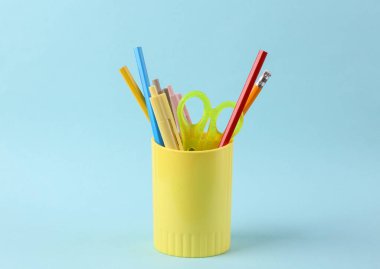 Renkli kalemler ve okul için mavi arka planda tutucu ya da bardak şeklinde çeşitli renkli kağıtlar.