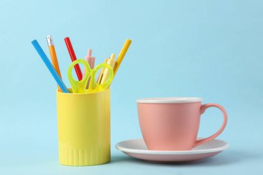 Kırtasiyeli plastik bardak, çizim araçları ve mavi arka planda bir fincan çay..