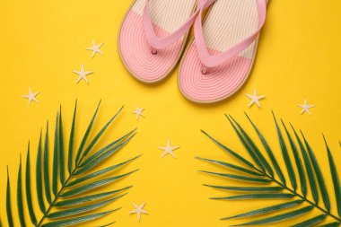 Yeşil palmiye yapraklı renkli parmak arası terlikler, mavi-pembe pastel arka planda deniz yıldızı. Plaj tatili, tropik konsept. Düz yatıyordu