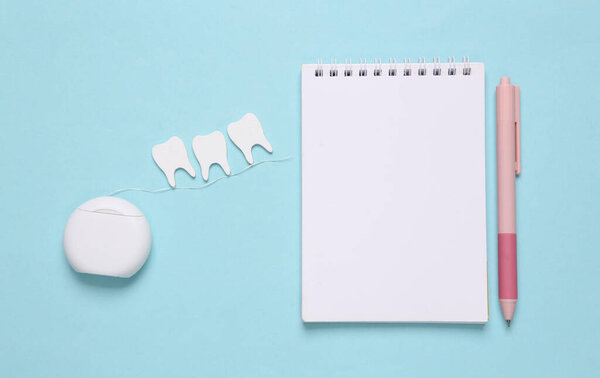 Dental care concept. Dental floss with teeth and notebook on blue background. Top view. Flat lay