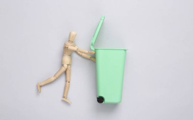 Tahta kukla gri arka planda boş çöp kutusu yuvarlar. Çöpçü.