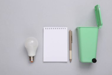 Ampullü oyuncak çöp tenekesi ve gri arka planda defter. Geri dönüşüm, ekolojik kavram. Üst manzara, düz uzanma