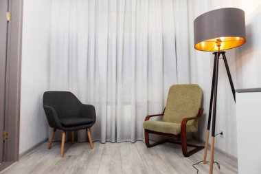 Perdeleri olan küçük odada iki koltuk ve lamba.