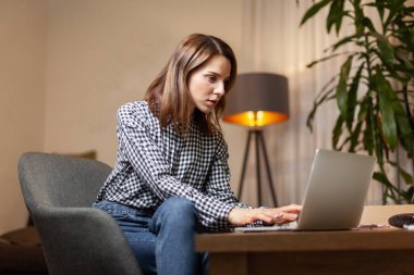 Genç ve çekici bir kadın evinde dizüstü bilgisayar kullanıyor.