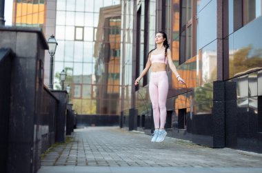 Bir şehir binasının arka planında ip atlama pratiği yapan zinde bir kadın. Sağlıklı bir yaşam tarzı. Kardiyo çalışması