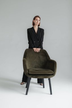 Stüdyoda siyah takım elbiseli, koltuklu genç bir kadının moda çekimi. Vogue, Yaşam Tarzı