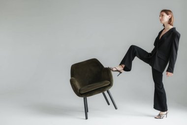 Stüdyoda siyah takım elbiseli, koltuklu genç bir kadının moda çekimi. Vogue, Yaşam Tarzı