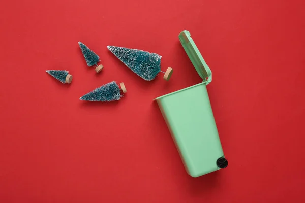 Kırmızı arka planda Noel ağaçları olan minyatür çöp kutusu. Noel çöp geri dönüşümü konsepti