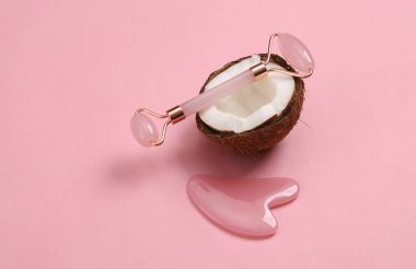 Yüz masajı silindiri ve pembe arka planda hindistan cevizi. Doğal kozmetik konsepti. Cilt bakımı