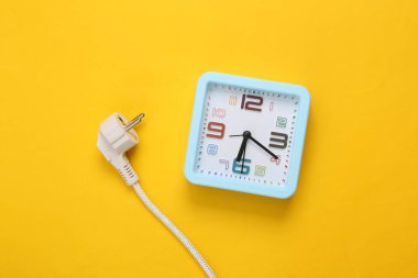 Sarı arkaplanda alarm saati olan elektrik prizi