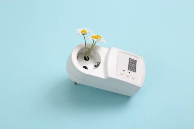 Eko konsepti. Mavi arka planda papatya çiçekleri olan elektrik prizi.