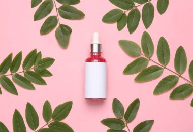 Pembe arka planda yeşil yapraklı bir şişe yüz serumu. Doğal kozmetik konsepti 