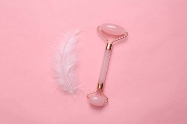 Facial massage roller with soft feather on pink background. Beauty layout