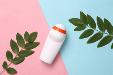 Antiperspirant roller with green leaves on blue pink background. Top view