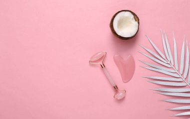 Facial massage roller with white palm leaves and coconut on pink background. Beautiful layout