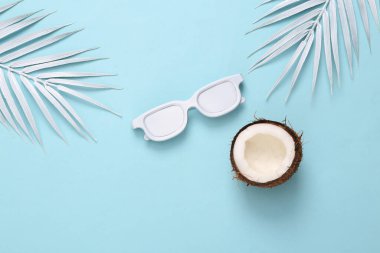 White sunglasses, coconut and palm leaves on blue background. Minimal travel, tropical layout. Top view