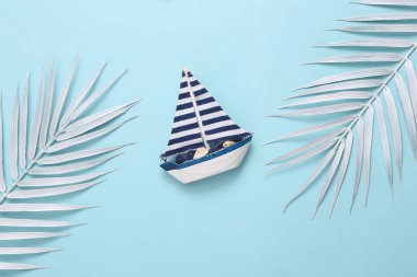 Yacht model and white palm leaves on blue background