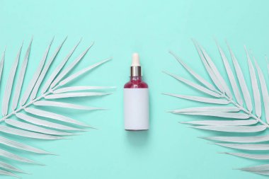 Turkuaz arka planda beyaz palmiye yaprakları olan yüz serumu şişesi.