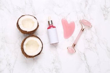 Bir şişe yüz serumu, masaj rulosu ve mermer arka planda hindistan cevizi. Üst görünüm