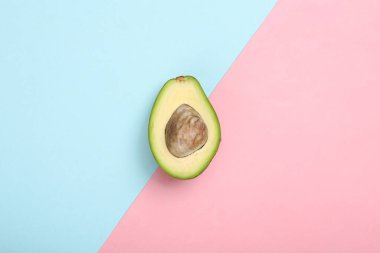 Mavi-pembe pastel arka planda olgun avokado meyvesinin yarısı. Üst görünüm
