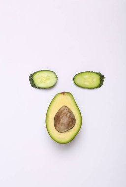 Creative composition of cucumber and avocado slices in the shape of face on white background