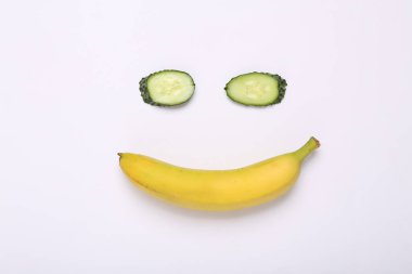 Creative composition of cucumber and banana in the shape of face on white background