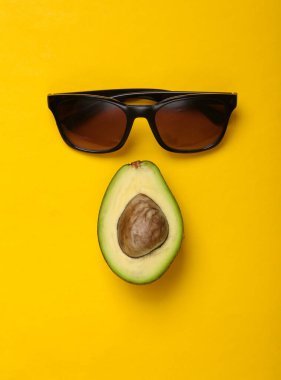 Sarı arka planda güneş gözlüğü ve avokado meyvesi. Üst görünüm, en düşük bileşim