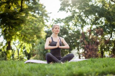 Genç bir kadın parkta mindere oturmuş meditasyon yapıyor. Yoga alıştırması..