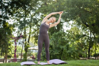 Genç ve çekici sarışın kadın parkta yoga pozu veriyor.