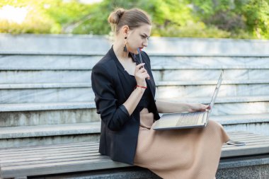 Parktaki bankta otururken dizüstü bilgisayar kullanan konsantre iş kadını.