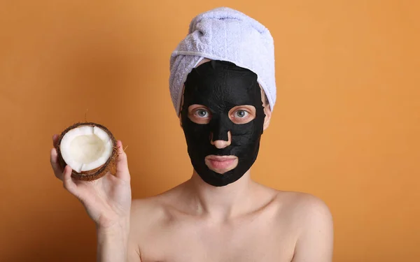 얼굴에 마스크를 머리에 타월을 아름다운 여성입니다 코코넛을 주황색 화장품 — 스톡 사진