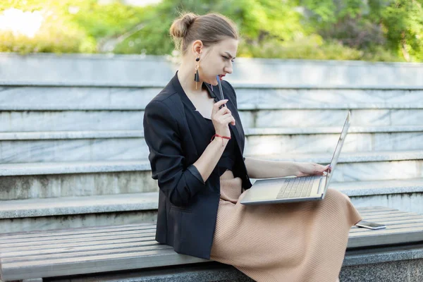 Parktaki bankta otururken dizüstü bilgisayar kullanan konsantre iş kadını.