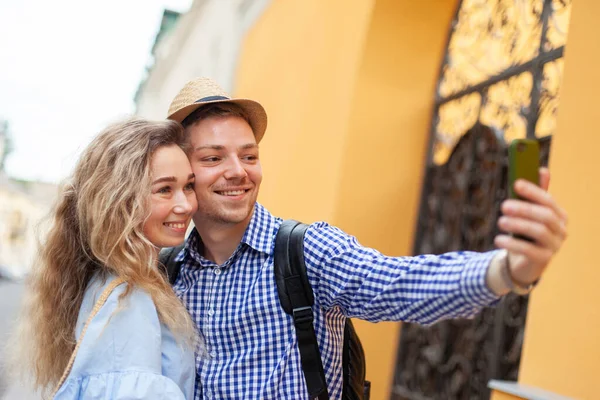 Genç bir çift Avrupa caddesinde akıllı telefondan selfie çekiyor.