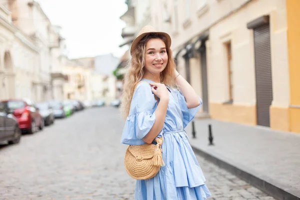 stock image Cute young woman in a hat and dress has fun on European street