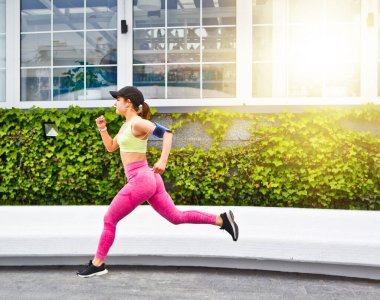 Spor giyim sektöründe kasıtlı olarak koşan ve müzik dinleyen genç bir kadın. Sabah koşusu. Fitness konsepti