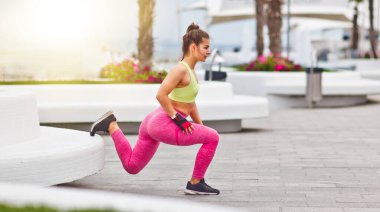 Genç ve çekici bir kadın şehir ortamında tek bacaklı egzersizler yapıyor.