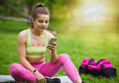 Parkta minderde otururken akıllı telefondan arkadaşlarıyla sohbet eden genç bir kadın.