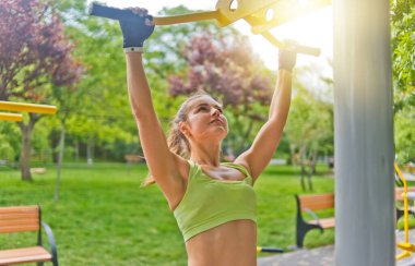 Genç bir kadın kendini parktaki yatay bir çubuğa çekiyor.