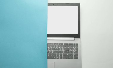 Dizüstü bilgisayarın yarısı plan kağıdının arkasına gizlenmiş. Minimalizm kavramı. Üst görünüm
