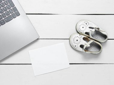 Fotokopi alanı için beyaz kağıt parçalı dizüstü bilgisayar ve tahta arka planda çocuk sandaletleri, üst manzara. Anneler Günü konsepti