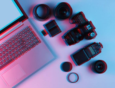 Ekipman profesyonel fotoğrafçısı. Laptop, kamera, lensler, flaşlar, ışık filtreleri. Neon ışığı. Arıza etkisi. Üst görünüm